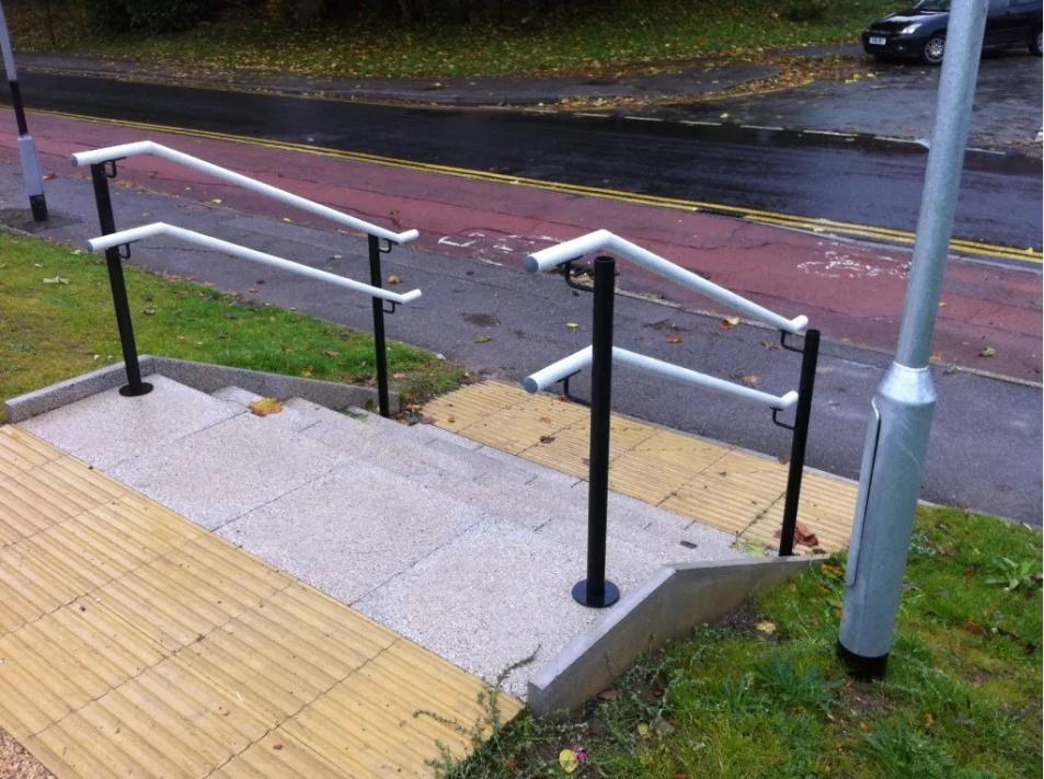 Twin rail external handrails with black powder coated posts and white powder coated rails beside tactile paving in Sheffield